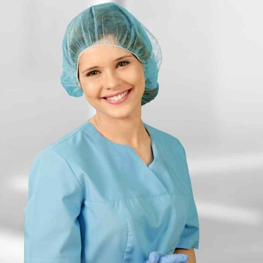 Smiling female healthcare professional in blue scrubs and hair cap.