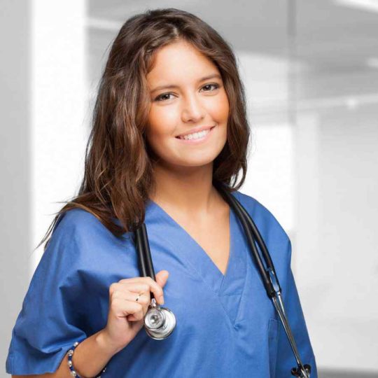 Smiling female nurse in blue scrubs with stethoscope.