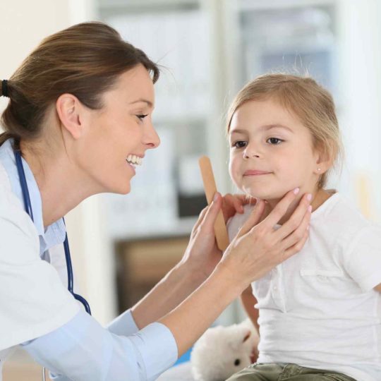 Doctor examining a young girl's throat during a check-up.