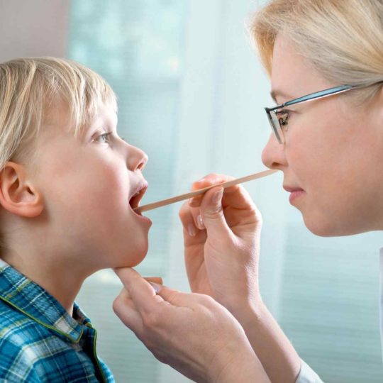 Doctor examining a young boy's throat with a tongue depressor.