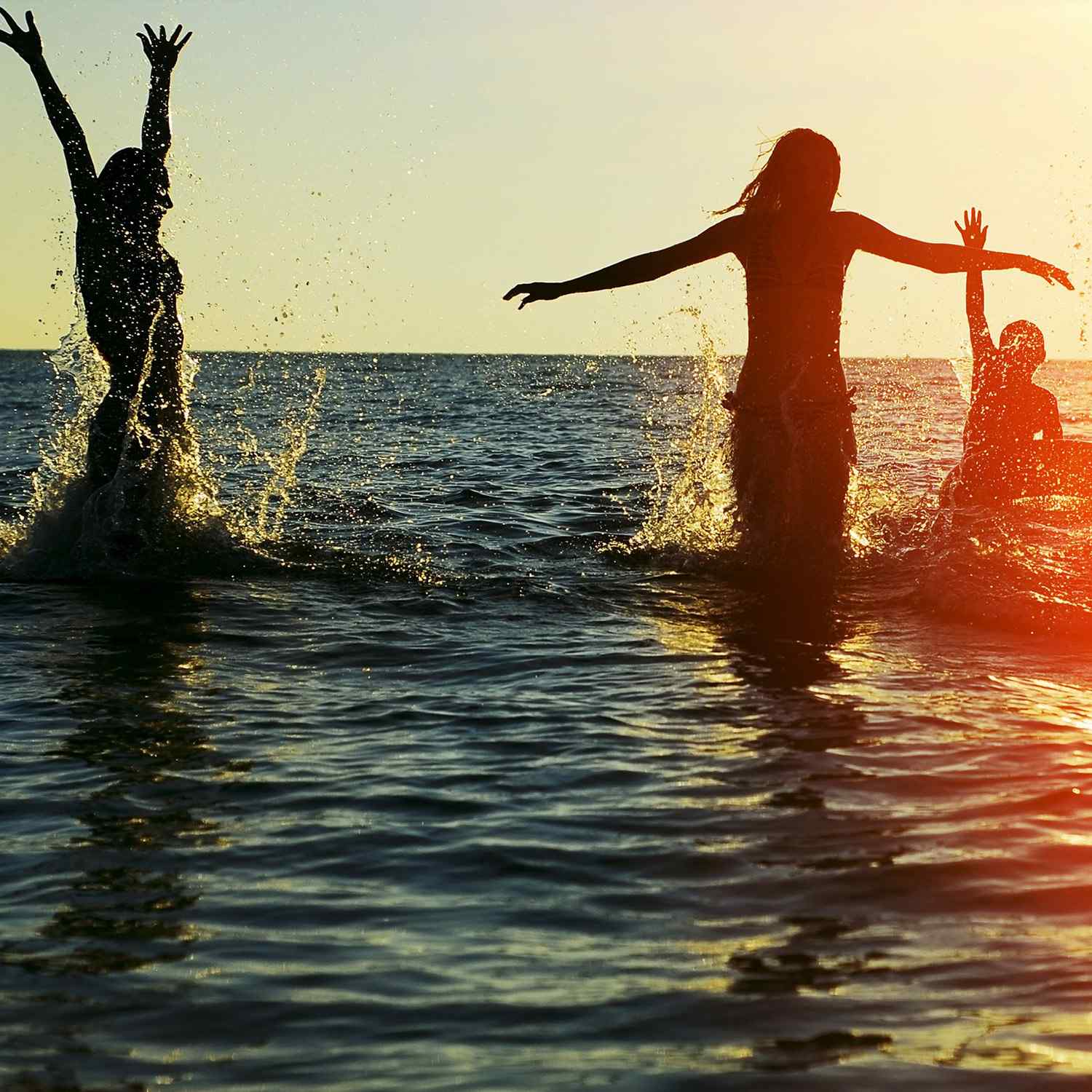 Three people joyfully playing in shallow ocean water during sunset.