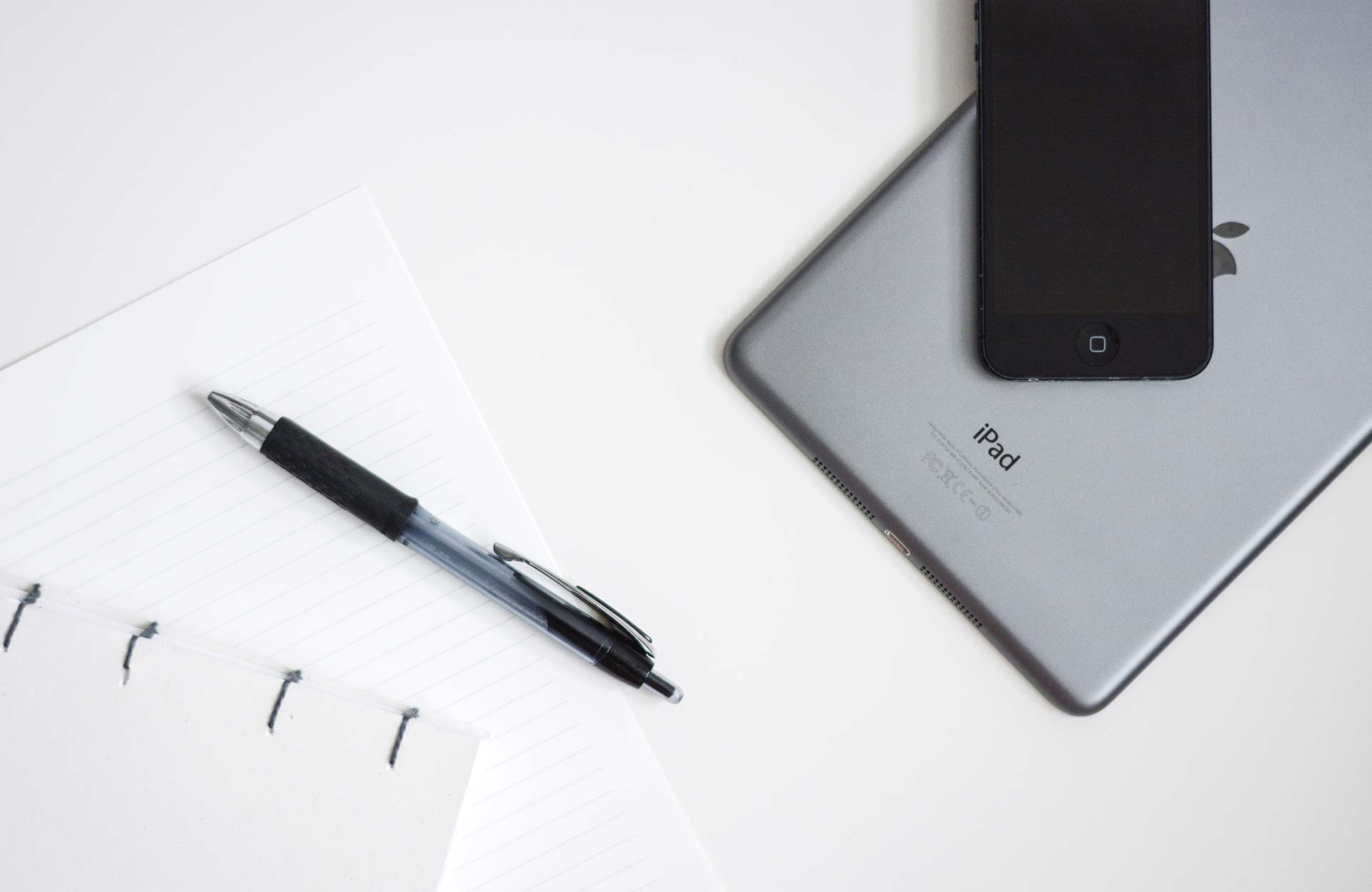 Notebook, pen, iPad, and smartphone on desk.