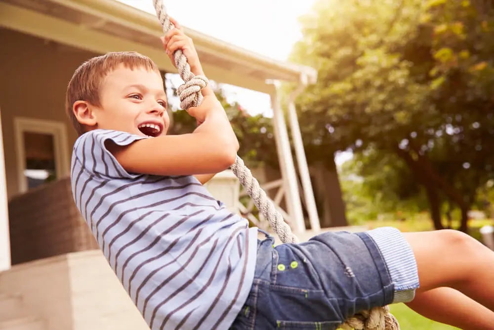 Boy joyfully swinging on a rope swing outdoors.